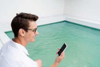 A man using smart phone besides an indoor pool